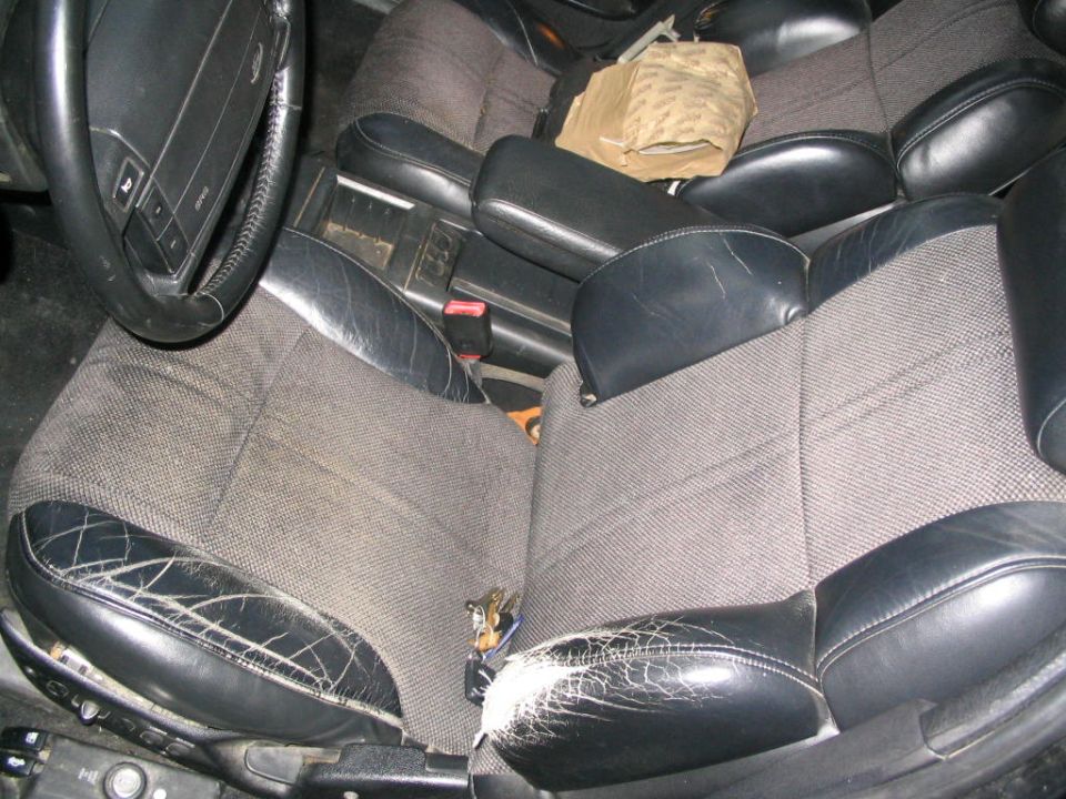 Interior shot of a car with worn leather and fabric seats, a steering wheel, and a center console