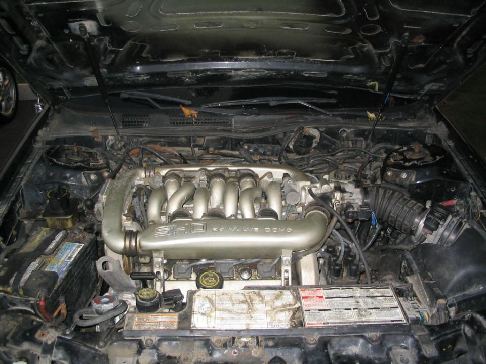 Engine bay of a 1990 Ford Taurus SHO, showing the V6 engine with intake manifold and battery