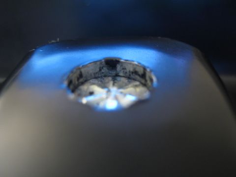 1990 Ford Bronco - extreme close-up of a worn circular metal lock or ignition cylinder lit with blue light.