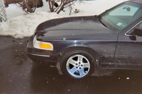 2000 Ford Crown Victoria - The front quarter panel and wheel of a dark sedan are visible in this snowy outdoor setting.