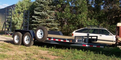 1990 Ford Bronco - A car trailer is parked outdoors with a white station wagon loaded onto its deck.