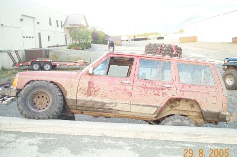 1988 Jeep Cherokee - Mud-covered 1988 Jeep Cherokee navigating an off-road obstacle.