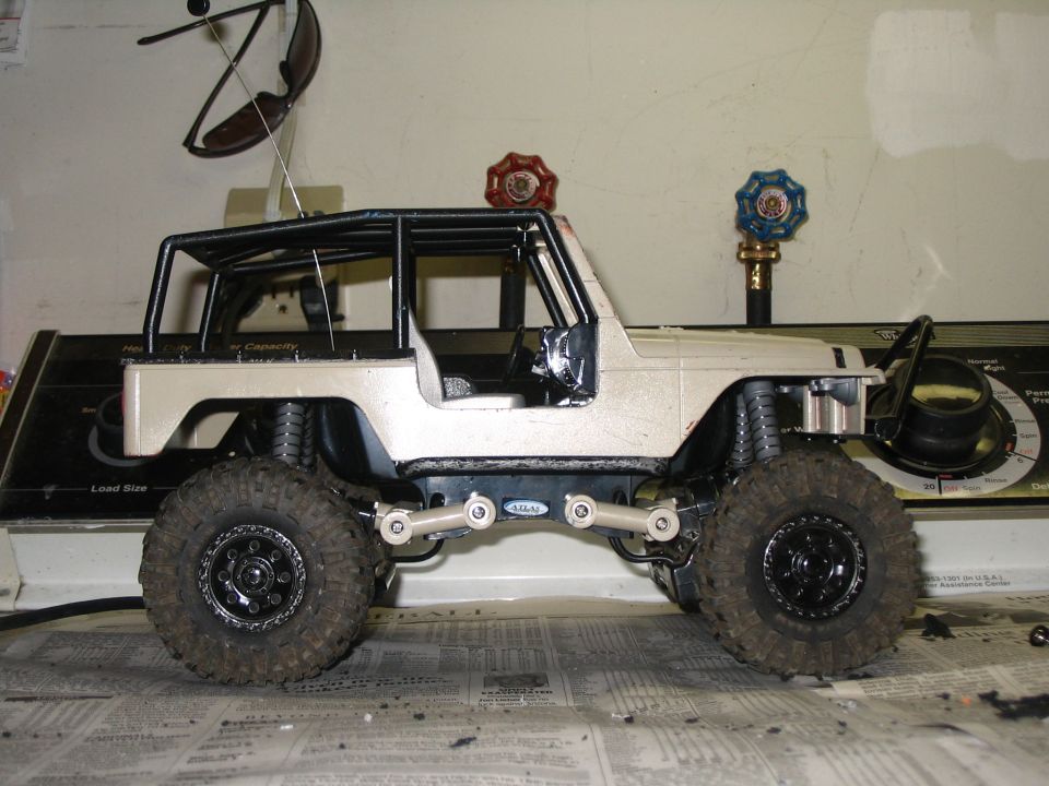Side view of tan RC crawler with roll cage and mud tires on a workbench