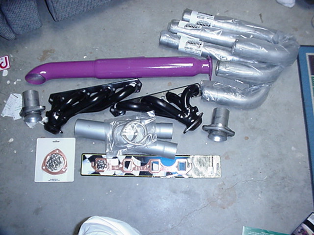 Various exhaust pipes, headers, and gaskets laid out on a concrete floor