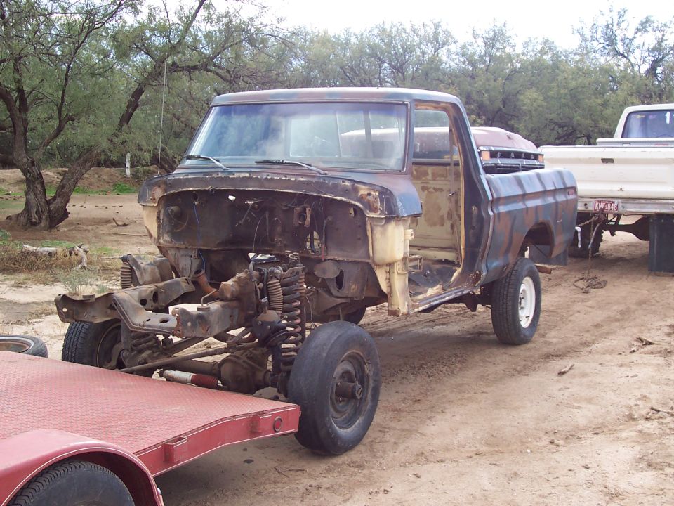 Rusty stripped pickup cab and bed on bare frame outdoors with desert trees
