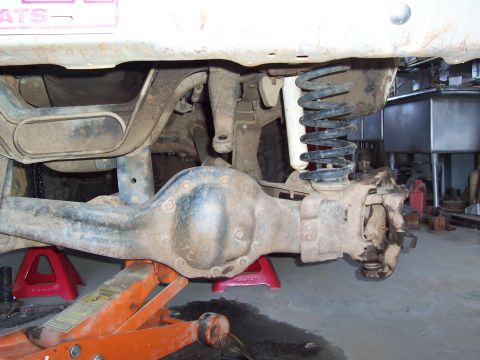 1981 Ford F-150 - Underside view of a solid front axle assembly on a lifted truck, showing the cast differential housing, coil spring, steering knuckle, and…