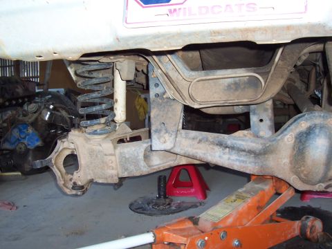 1981 Ford F-150 - Underside view of a lifted Ford truck's front suspension, showing a solid front axle, coil spring, shock absorber, and steering knuckle, wi…