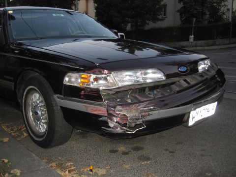 1992 Ford Crown Victoria - This dark sedan, identified as a 1992 Ford Crown Victoria, shows significant damage to its front bumper.