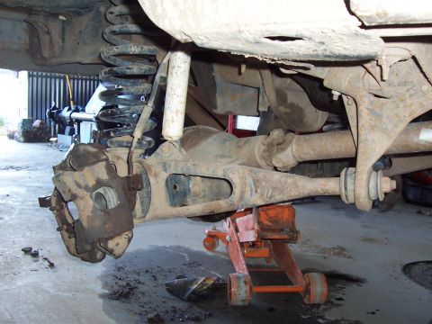 1981 Ford F-150 - Underside view of a truck's front solid axle showing the differential, front driveshaft with U-joint, coil spring suspension, and a dust-co…