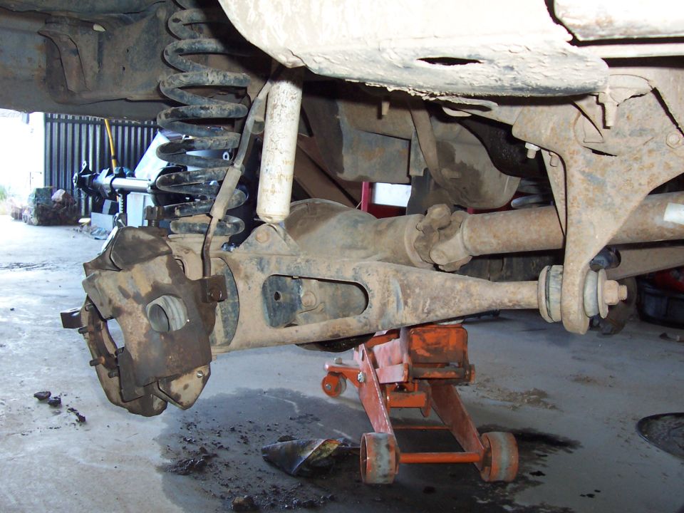Underside of truck front solid axle with differential, coil spring, and brake caliper on floor jack