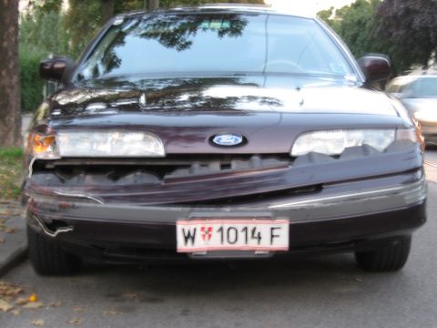 1992 Ford Crown Victoria - The front of a dark purple 1992 Ford Crown Victoria shows significant damage to the bumper and grille.