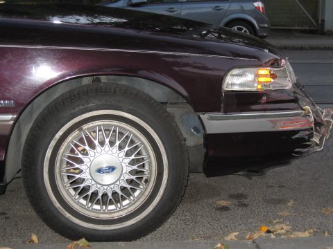 1992 Ford Crown Victoria - Front quarter view of a damaged 1992 Ford Crown Victoria, showing the fender and bumper. Another vehicle is visible in the background.