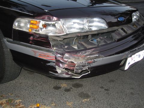 1992 Ford Crown Victoria - The front of a dark sedan shows significant damage to the bumper and headlight area.