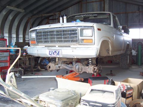 1981 Ford F-150 - A white 1980s Ford F-150 pickup viewed from the front three-quarter angle, raised on jack stands with the front differential, leaf springs…