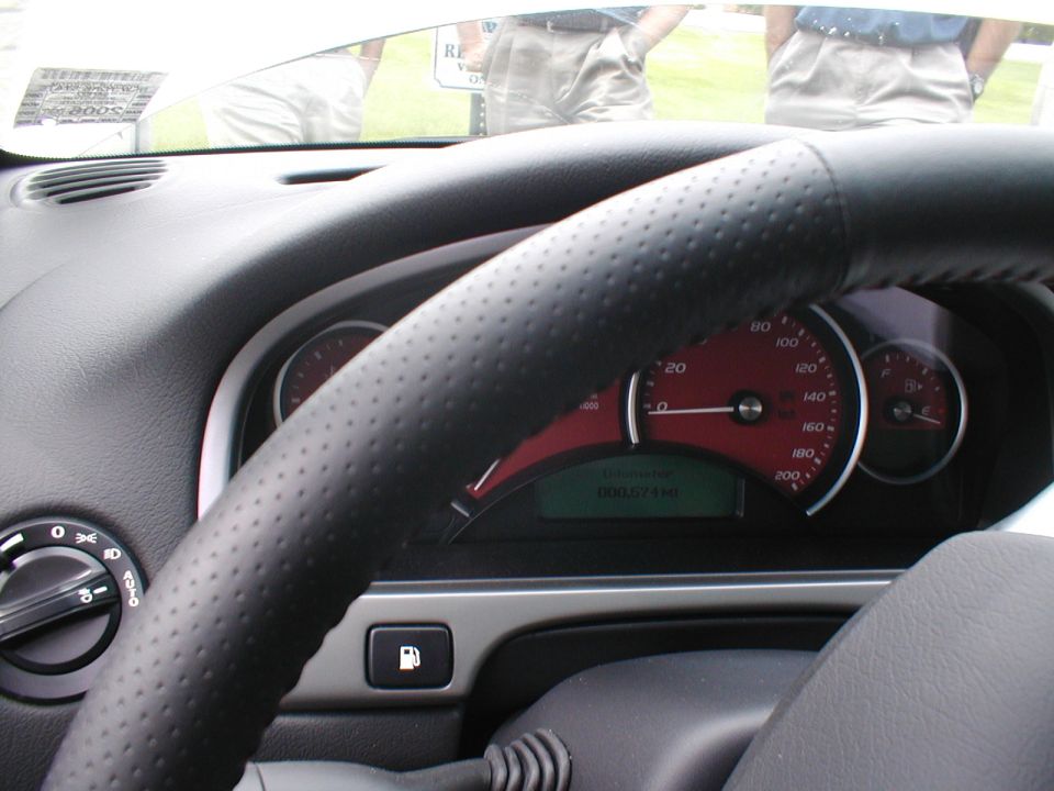 Steering wheel and dashboard of a car with red gauges. Odometer reads 000571 km