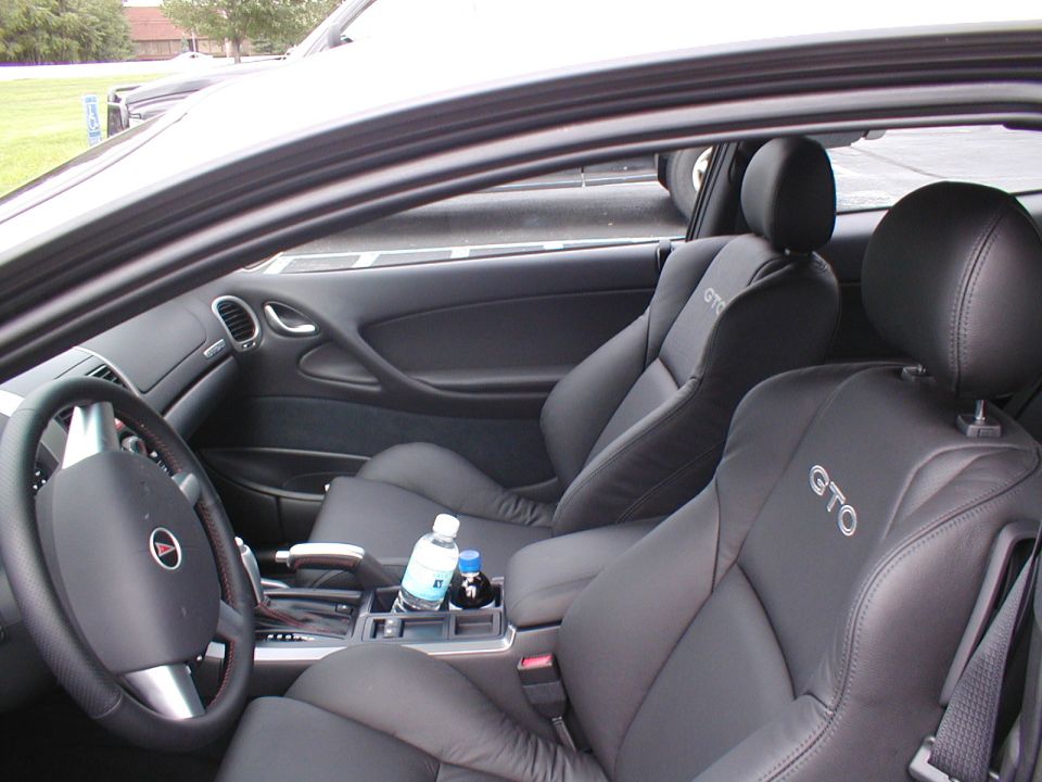 Black leather car seats with 'GTO' stitched on headrests, center console with water bottles
