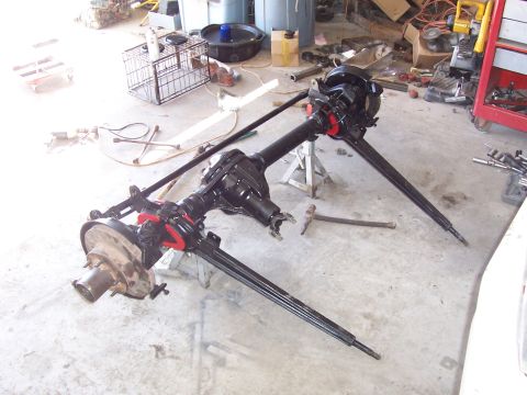 1981 Ford F-150 - Two removed solid front axles with differentials and axle shafts laid out on a garage floor, featuring painted black housings with red-pain…