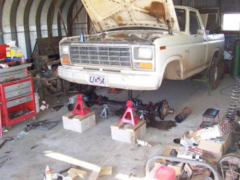 1981 Ford F-150 - A white Ford F-150 pickup sits in a garage with its hood up and front end raised on red jack stands atop concrete blocks, exposing the fron…