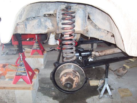 1981 Ford F-150 - Close-up of a front suspension and brake assembly on a vehicle raised on red jack stands, showing a coil spring with orange/red paint, a bl…