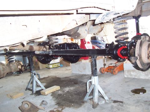 1981 Ford F-150 - Underside view of a truck's front solid axle supported on two aluminum jack stands, showing a freshly painted black axle housing, coil spri…