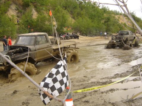 1987 Suzuki Samurai - Two trucks are stuck in a muddy off-road course, with a checkered flag signaling the end of the race.