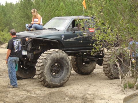1987 Suzuki Samurai - This heavily modified truck features oversized tires and a custom roll cage, with a woman perched on its hood.