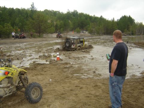 1987 Suzuki Samurai - Off-road vehicles are navigating a muddy track with trees in the background.