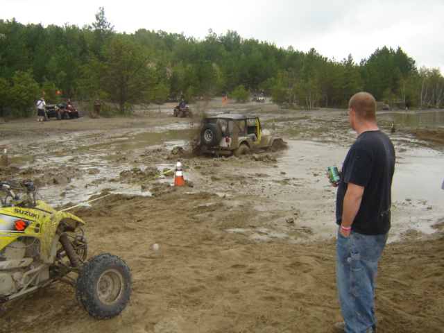 ATVs and a Jeep stuck in mud, with people watching