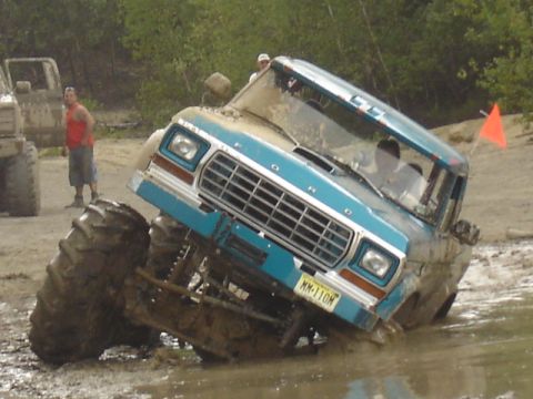 1987 Suzuki Samurai - A modified Ford truck navigates a muddy obstacle course with another vehicle in the background.
