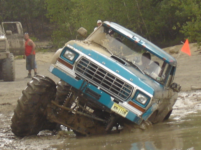 Blue Ford F-Series truck with oversized tires stuck in mud, front grille visible