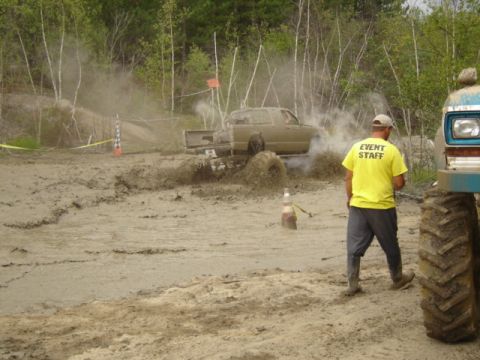1987 Suzuki Samurai - Mud bogging event with a pickup truck struggling through the mire. An event staff member is present.