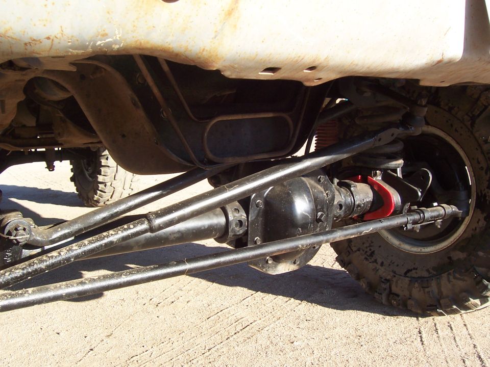 Underbody close-up of front axle, drag link and red steering stabilizer on a lifted truck
