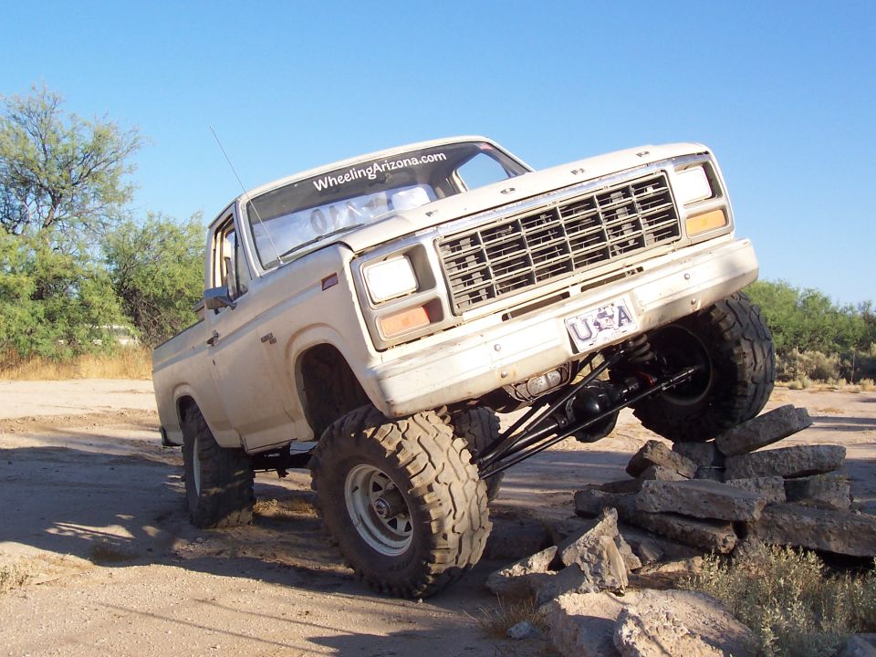 White lifted Ford truck with chrome grille flexing front tires over rocks
