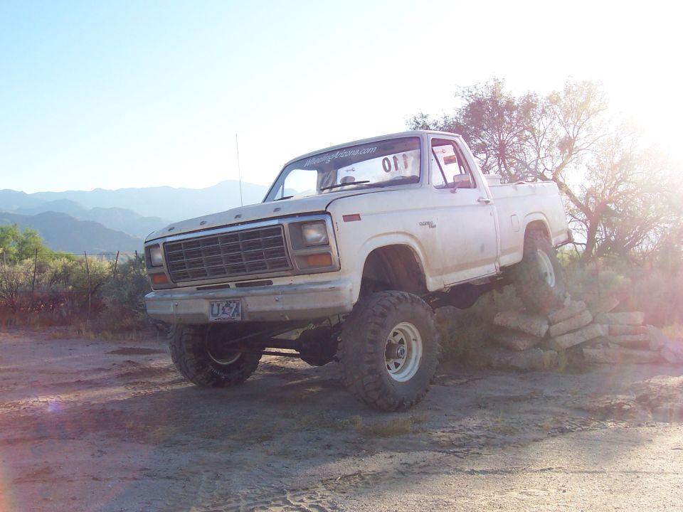 White lifted Ford pickup on rocks at dusk with mountains and lens flare behind