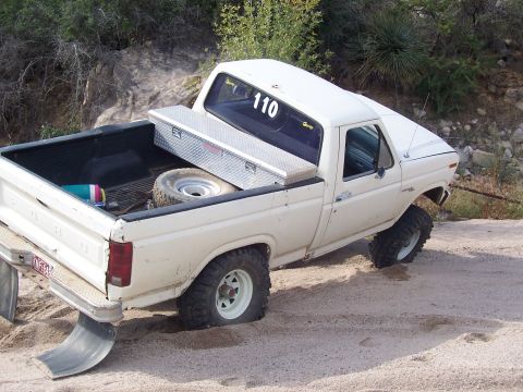 1981 Ford F-150 - This white 1980s Ford F-150 pickup truck is stuck in the sand, with the number 110 visible on its rear window.