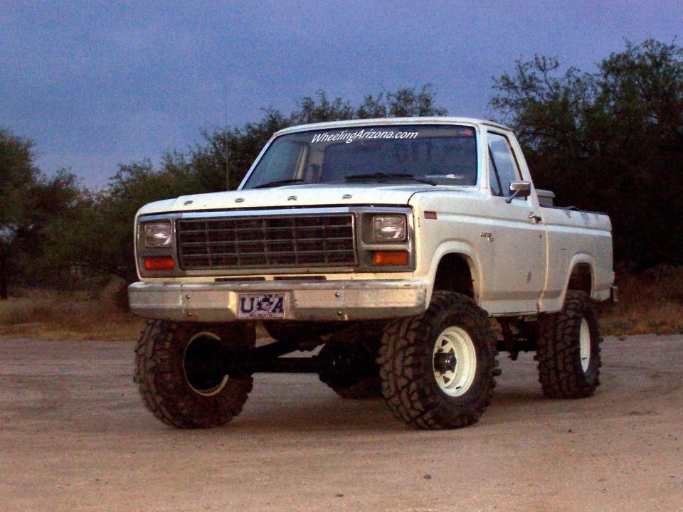 White lifted Ford pickup front three-quarter on dirt at dusk with big mud tires