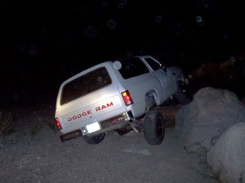 1981 Ford F-150 - Dodge Ram pickup truck is shown off-roading at night, climbing over rocks.