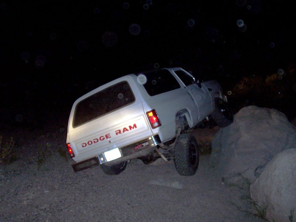 White lifted Dodge Ram Ramcharger climbing a boulder at night, rear three-quarter view