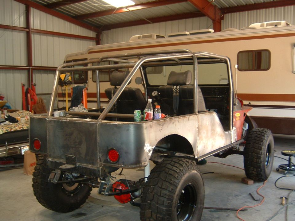 Bare-metal Jeep CJ project with roll cage and big tires in a shop