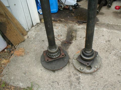 1979 Ford Bronco - Two axle shafts with hubs are shown resting on a concrete surface.