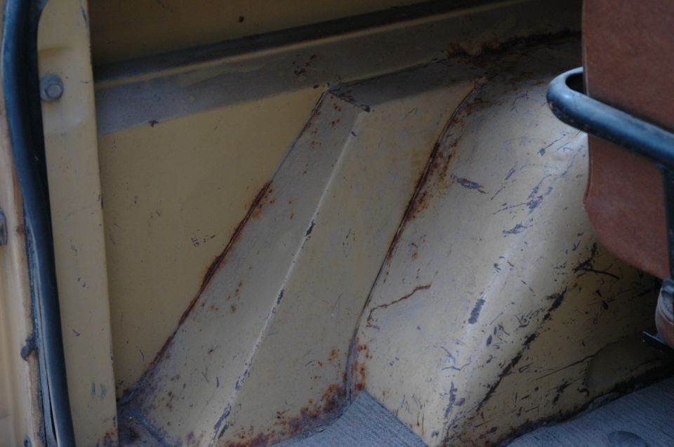 Rusty cream-painted rear cargo area and wheel well inside a vintage 4x4, red vinyl seat at right
