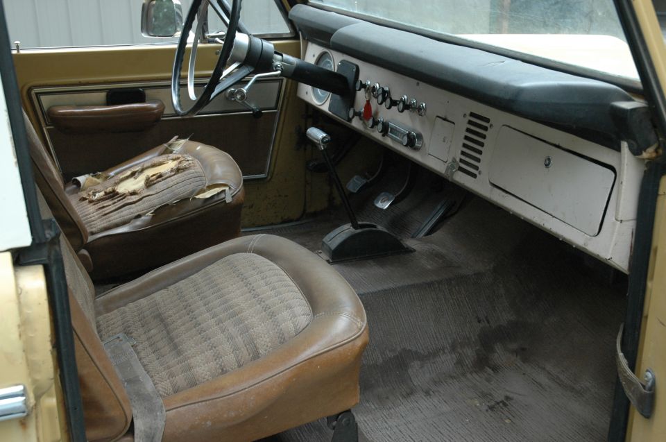 Worn tan and brown interior of a vintage Ford Bronco with torn seat and metal dash