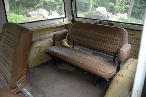 1972 Ford Bronco - The interior of a 1972 Ford Bronco shows the rear bench seat and the side seat, with a view of the outdoors through the windows.