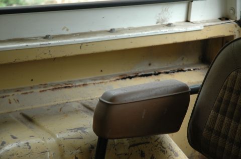 1972 Ford Bronco - The interior of the vehicle shows signs of wear and rust, with a close-up on the passenger seat and armrest.