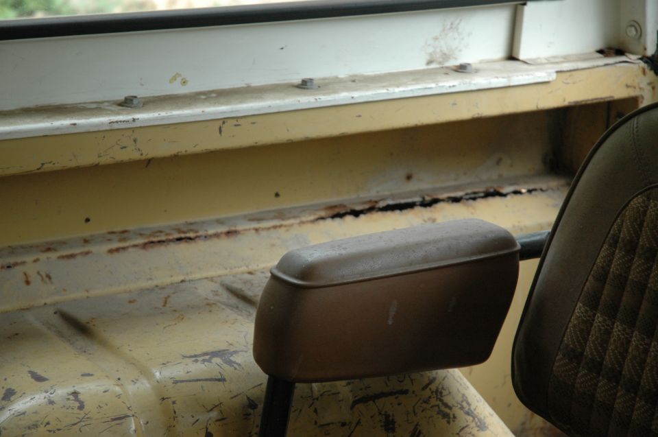 Interior view of a vehicle's passenger side, showing a worn seat and rusted metal