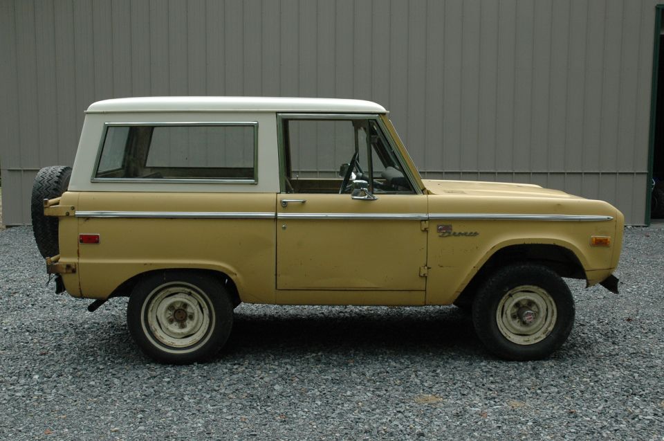 Side view of a yellow 1972 Ford Bronco with a white hardtop and spare tire on the back