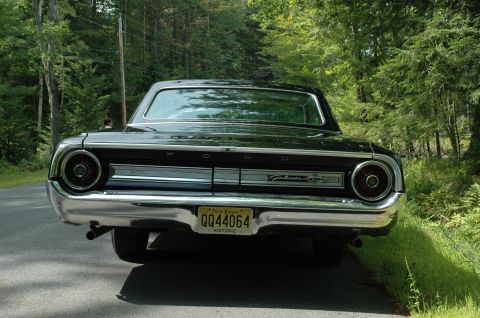 1964 Ford Galaxie - Rear view of a black 1964 Ford Galaxie 500XL parked on a wooded road, displaying its distinctive taillights and chrome bumper.