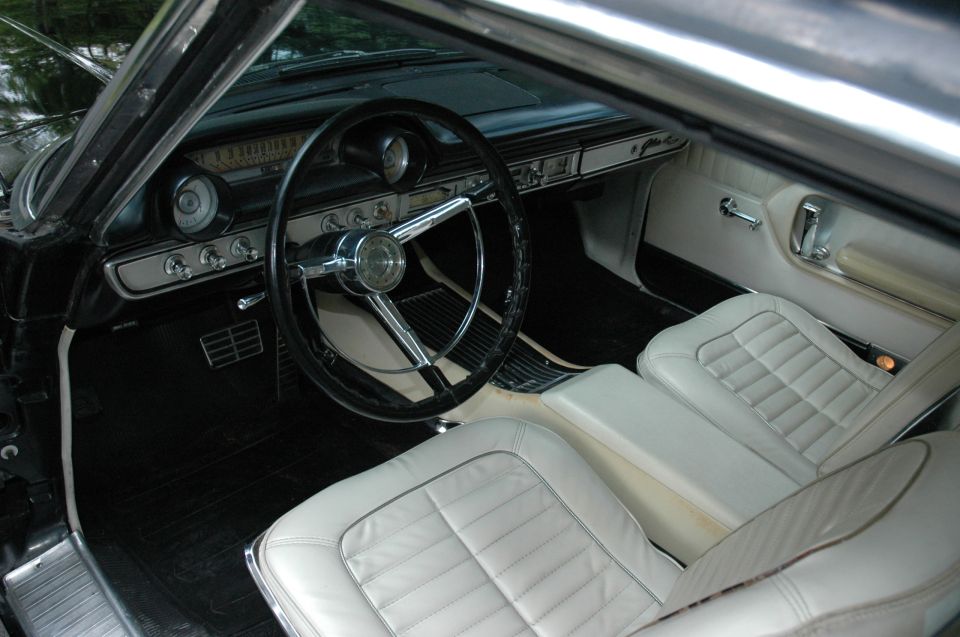 1960s Ford interior with white vinyl bucket seats, black dash and chrome-hub steering wheel
