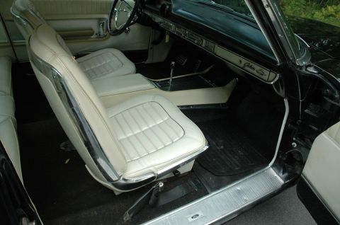 1964 Ford Galaxie - The interior of a 1964 Ford Galaxie 500XL features white vinyl bucket seats and a black dashboard with chrome accents.