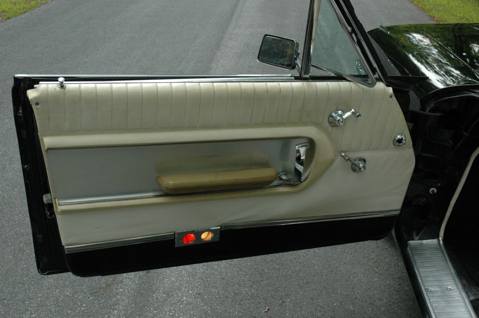 Open door of black classic car with white pleated vinyl panel and chrome crank